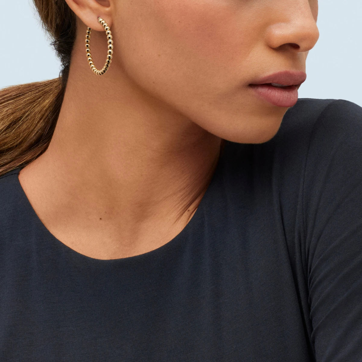 Profile of a model in a navy top wearing a large beaded gold hoop earring