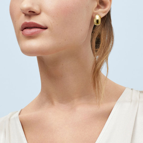 Close-up of a model in a white top wearing a thick, polished gold hoop earring