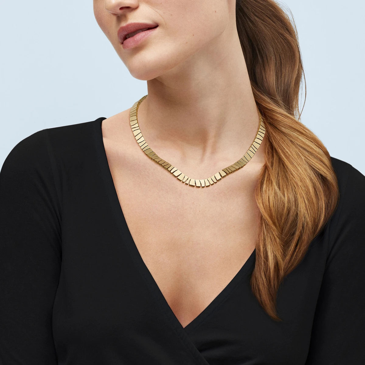 Model in a black V-neck wearing a gold collar of geometric links