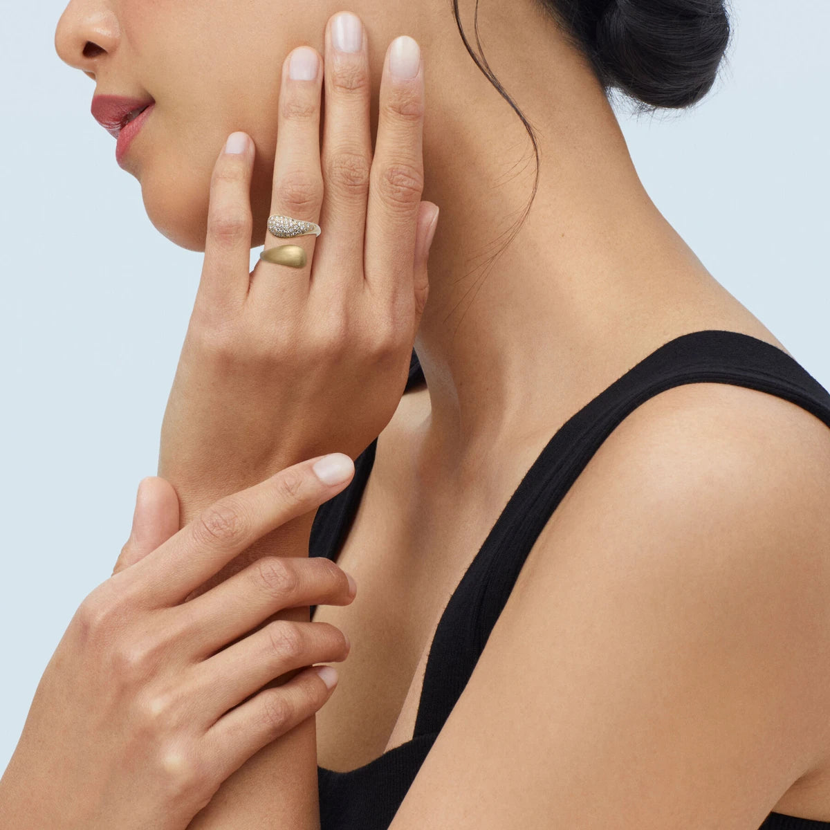 Model in a black top with a hand at the cheek, wearing an open gold ring with one end set with small diamonds