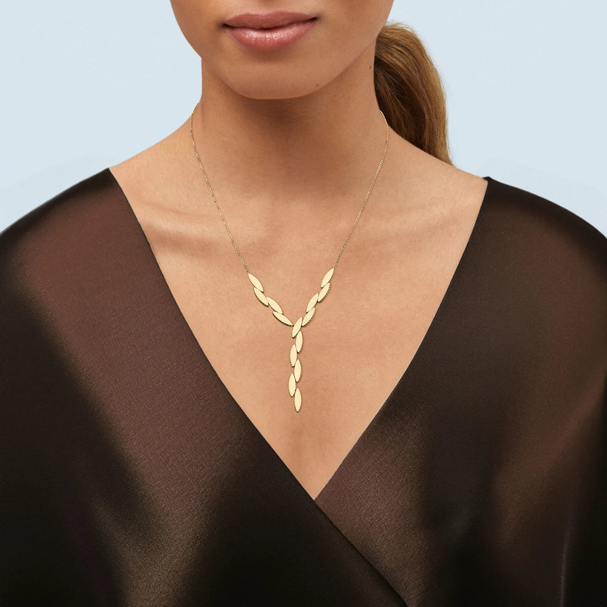 Model in a sheer dark brown wrap top wearing a gold Y-lariat necklace