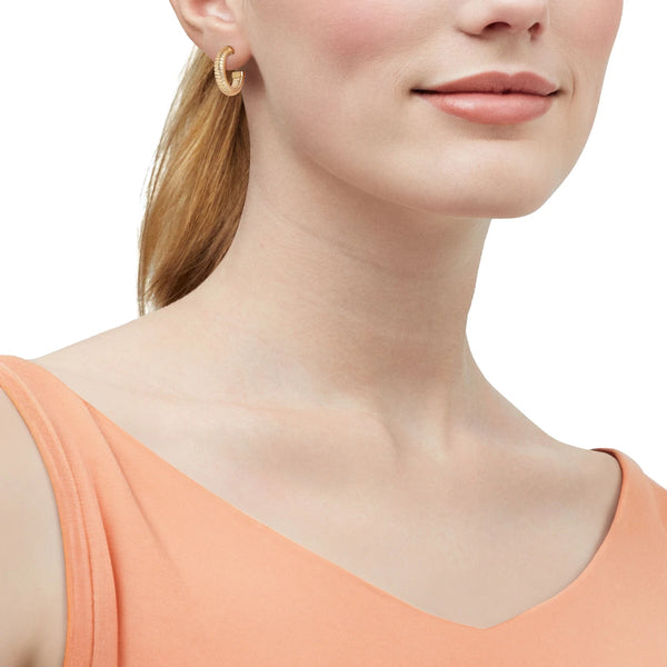 Model in a peach top wearing a small ribbed gold hoop earring